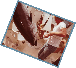 An old photo of cutting up a large fish while wearing a fishing shirt